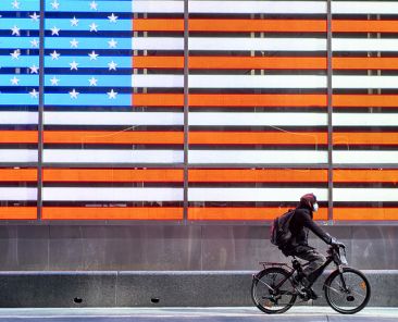 New York, United States, USA March 24, 2020: african american man with mask riding a bicycle in front of the united states flag in times square during coronavirus pandemic