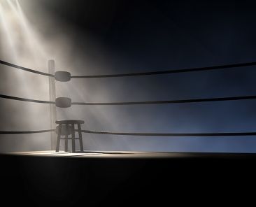 A dramatic view of the corner of an old vintage boxing ring with an empty stool spotlit by a single spotlight on an isolated dark background