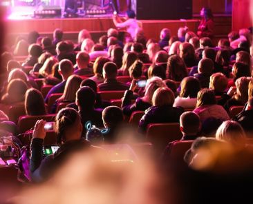 Spectators sit in the hall and watch a concert. People in the auditorium watching the performance. Theater audience. Music concert or festival. Out of focus